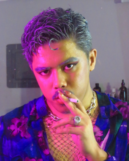 Guy with silver hair under pink lighting. He throws a sharp judging gaze towards the camera as he puts on a cigarette on his mouth while holding it with his index and middle fingers.