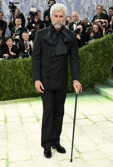 Bad Bunny wearing an all black outfit, a white hair wig, facial hair, and prosthesis to make him look 70 years old.