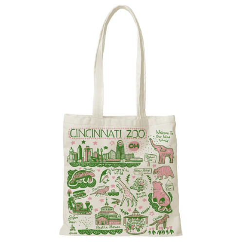 The image features a white tote bag adorned with a map of Cincinnati Zoo. The bag is embellished with various city illustrations, including a red train and a green giraffe. The bag has two handles, one on each side, which are also decorated with green and pink stars. The bag is placed on a white surface, and the overall scene appears to be a light-hearted and creative design.