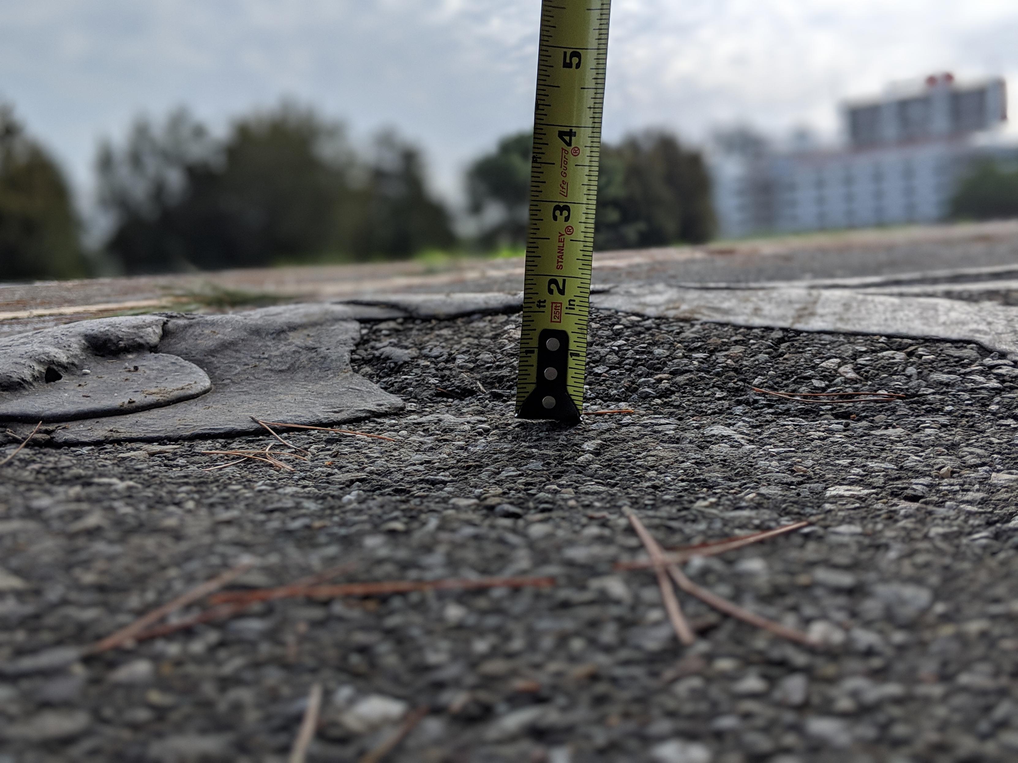 Tape measure measuring the height of a bump in the tar showing a 2" rise over a 6" run