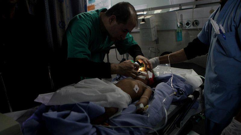 Picture of a doctor analyzing a young child, with bandages on a hospital bed, Using his cell phone light

Pic provided by @BajoOcupacion on X