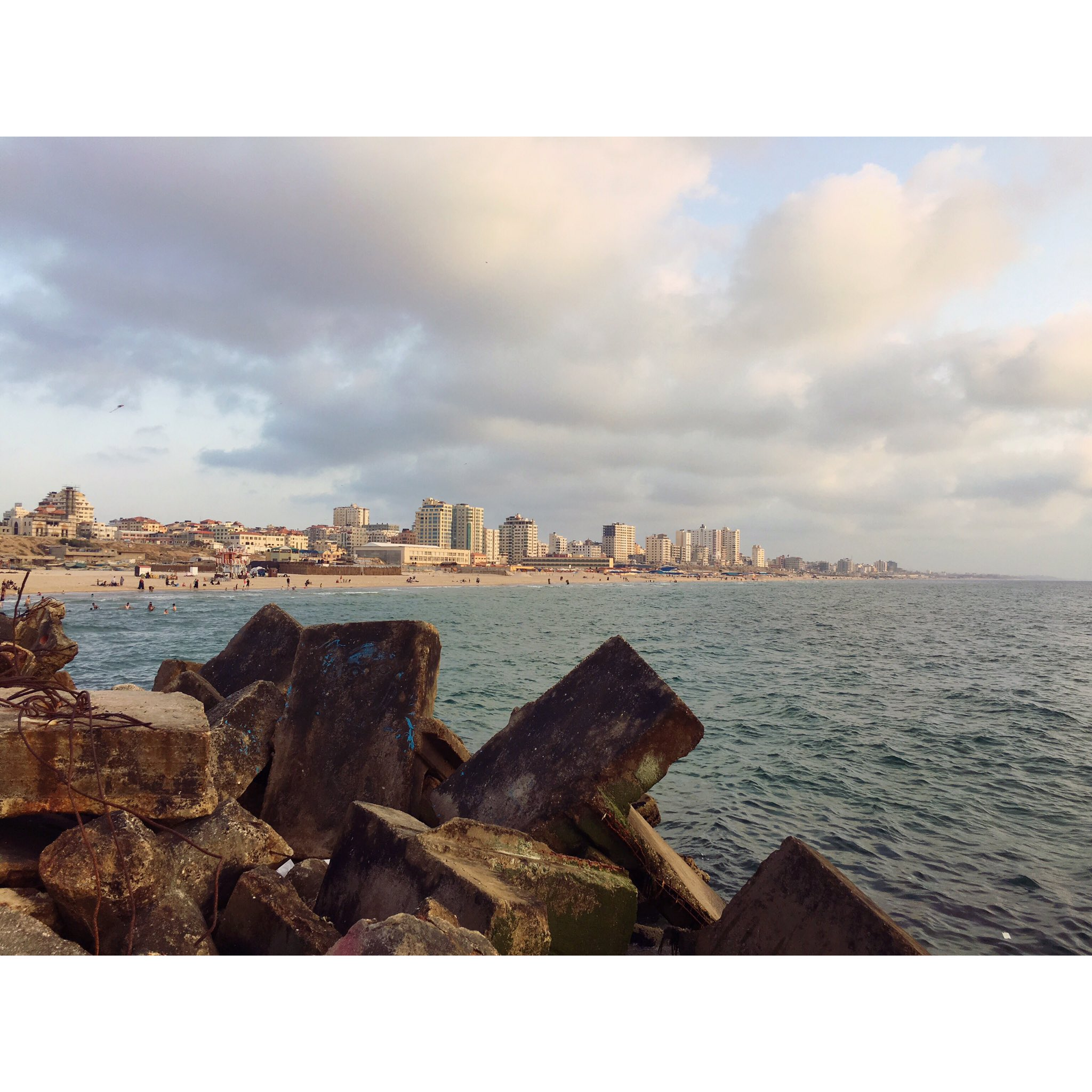 Pic provided by Farah Baker.

 Rocks in the forefront then a lot of the sea and in the distance we see the gaza beach with many people on it and some taller white buildings in the center.