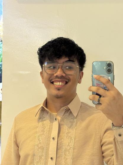 Man in a Barong Tagalog wearing a pair of glasses and smile as he takes a mirror selfie with his iPhone. Man in a Barong Tagalog wearing a pair of glasses and smile as he takes a mirror selfie with his iPhone.