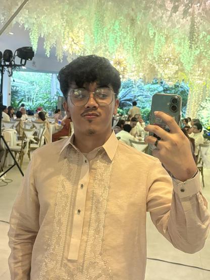 Southeast Asian man wearing a Barong Tagalog embroidered with intricate patterns taking another mirror selfie in a different part of a party venue. Southeast Asian man wearing a Barong Tagalog embroidered with intricate patterns taking another mirror selfie in a different part of a party venue.